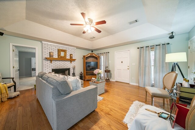 living room featuring a tray ceiling, a fireplace, light hardwood / wood-style floors, and a textured ceiling