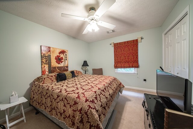 bedroom with ceiling fan, a closet, light carpet, and a textured ceiling