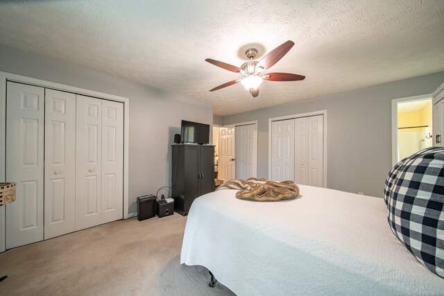 carpeted bedroom featuring multiple closets, ceiling fan, and a textured ceiling