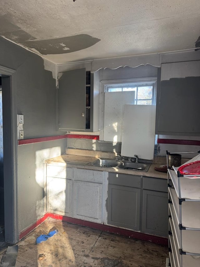 kitchen with a textured ceiling, concrete flooring, gray cabinetry, and sink