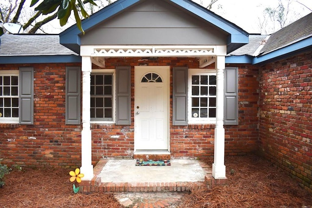 entrance to property with roof with shingles and brick siding