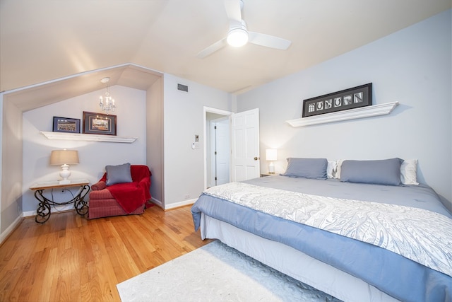 bedroom with vaulted ceiling, ceiling fan with notable chandelier, and wood-type flooring