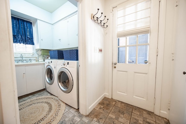 clothes washing area featuring sink, washing machine and clothes dryer, and cabinets