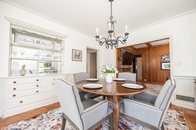 dining area with an inviting chandelier, crown molding, and wood walls