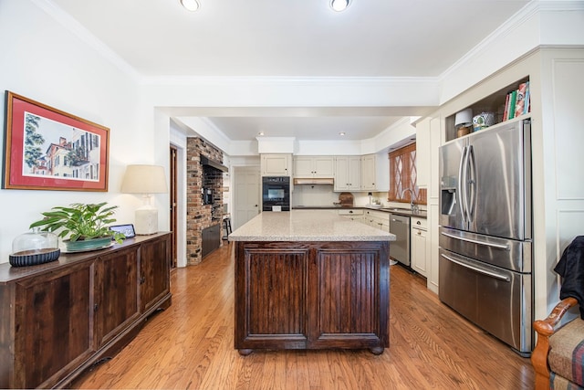 kitchen featuring light stone countertops, appliances with stainless steel finishes, a kitchen island, sink, and light wood-type flooring