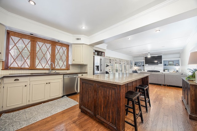 kitchen with light stone countertops, appliances with stainless steel finishes, a center island, sink, and cream cabinetry