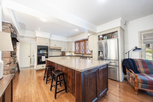 kitchen featuring stainless steel fridge with ice dispenser, double oven, light wood-type flooring, and a center island