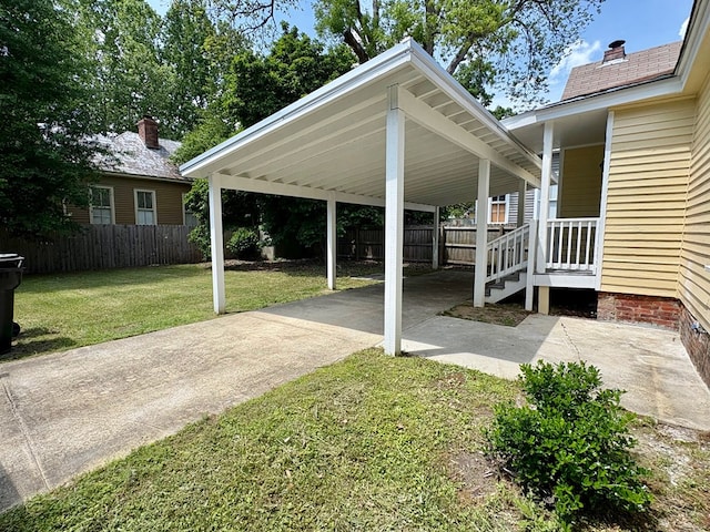 view of yard with concrete driveway, a carport, and fence