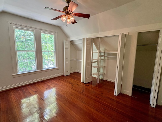 unfurnished bedroom featuring lofted ceiling, multiple closets, dark wood-style floors, and baseboards