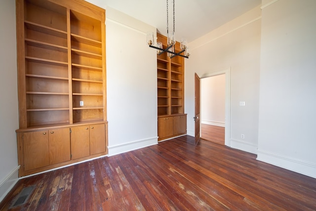 empty room with dark hardwood / wood-style flooring, a chandelier, and built in features