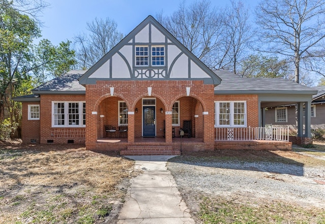 tudor home with a porch, brick siding, roof with shingles, and crawl space