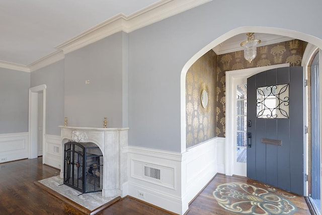 entrance foyer with arched walkways, a wainscoted wall, ornamental molding, dark wood-type flooring, and a fireplace