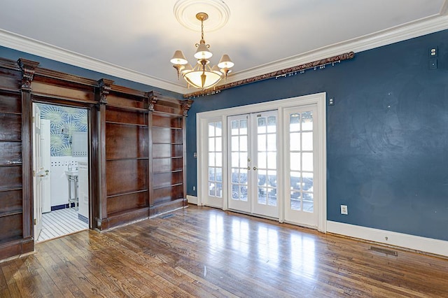 empty room featuring a notable chandelier, french doors, wood finished floors, and crown molding