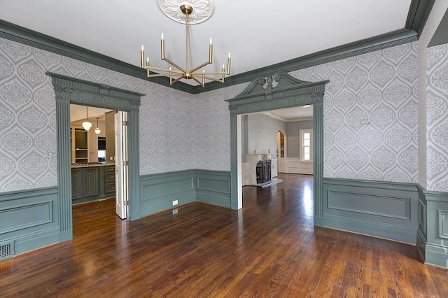 unfurnished dining area featuring a wainscoted wall, ornamental molding, a fireplace, and wallpapered walls