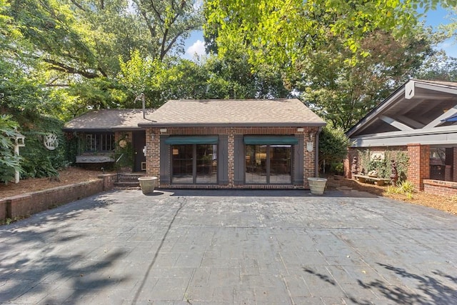 entrance to property featuring a patio area, roof with shingles, and brick siding