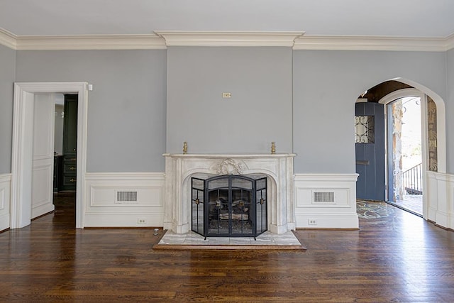 unfurnished living room featuring arched walkways, ornamental molding, dark wood-style flooring, and visible vents