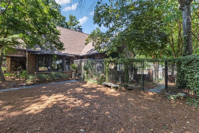 back of house featuring brick siding, roof with shingles, fence, and a sunroom