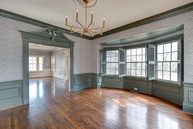 unfurnished room featuring wallpapered walls, wainscoting, crown molding, and an inviting chandelier