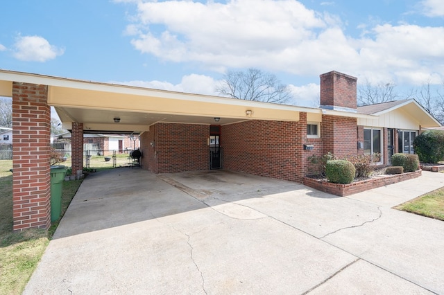 exterior space featuring driveway, a chimney, fence, a carport, and brick siding