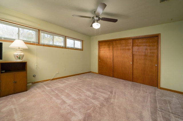 unfurnished bedroom with light carpet, ceiling fan, a closet, and baseboards