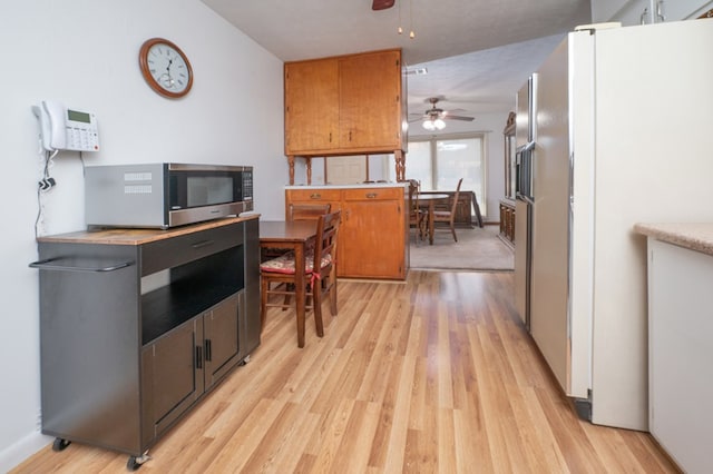 kitchen with ceiling fan, light wood-style floors, freestanding refrigerator, brown cabinets, and stainless steel microwave