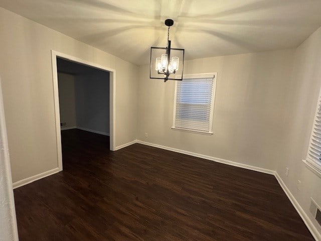 spare room with baseboards, a notable chandelier, and dark wood-style flooring