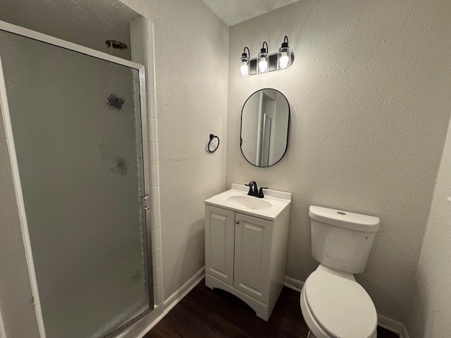 full bathroom with toilet, a stall shower, wood finished floors, vanity, and a textured wall