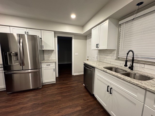 kitchen with light stone countertops, dark wood finished floors, a sink, appliances with stainless steel finishes, and white cabinetry