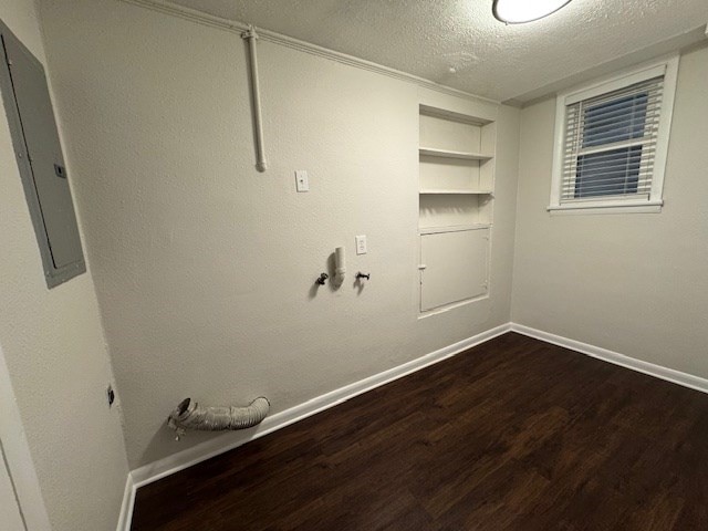 clothes washing area with built in shelves, baseboards, dark wood finished floors, electric panel, and a textured ceiling