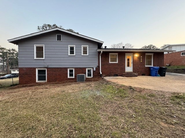 back of house with brick siding, a lawn, entry steps, and central AC