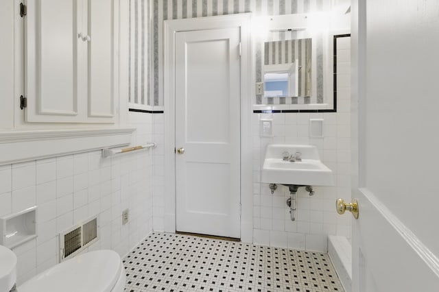 bathroom with tile walls, toilet, a wainscoted wall, and a sink