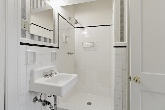 full bathroom with a tile shower, a sink, and tile walls