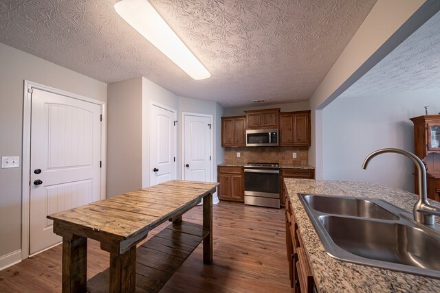37 Oakwood Dr, Phenix City, AL 36870 - kitchen featuring appliances with stainless steel finishes, dark wood-style flooring, a textured ceiling, backsplash, and brown cabinets