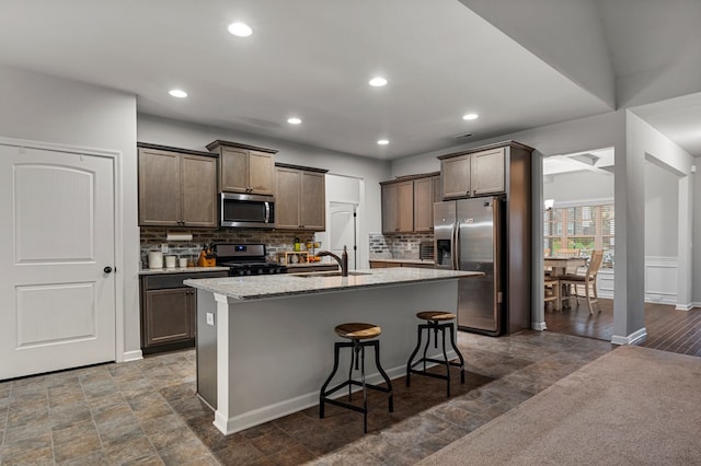 7546 Mockernut Way, Midland, GA 31820 - kitchen featuring appliances with stainless steel finishes, backsplash, a kitchen island with sink, light stone counters, and a kitchen bar
