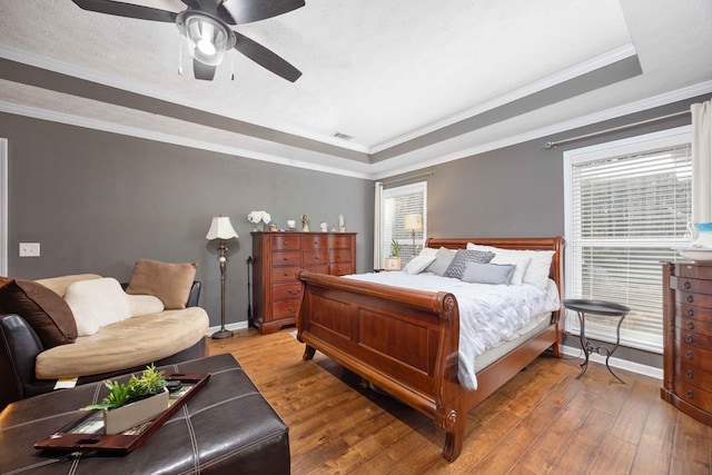 bedroom with baseboards, light wood-type flooring, a tray ceiling, visible vents, and ornamental molding