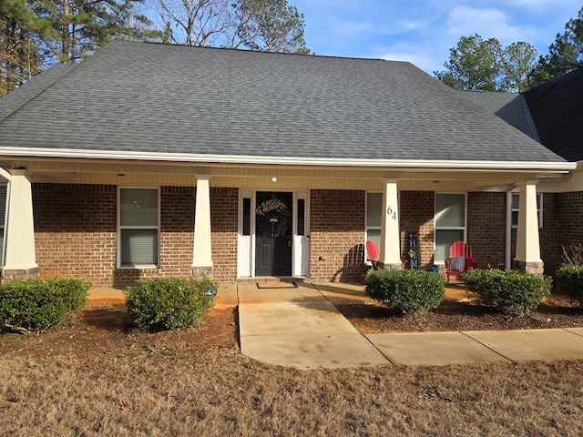 view of front facade with brick siding, roof with shingles, and covered porch