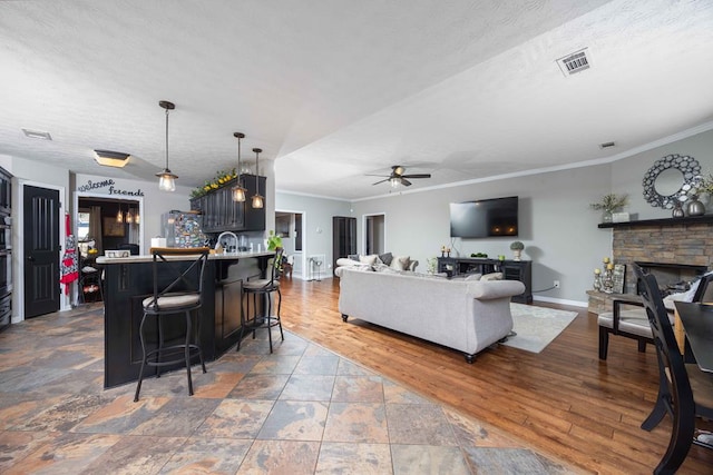 living area featuring a ceiling fan, visible vents, ornamental molding, and a fireplace