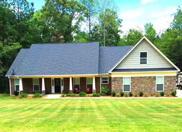 view of front of property featuring a front lawn, roof with shingles, covered porch, and stone siding