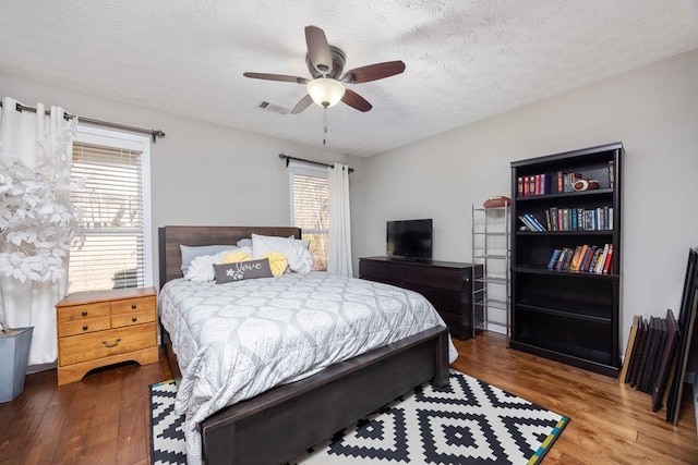 bedroom with a textured ceiling, visible vents, multiple windows, and wood finished floors
