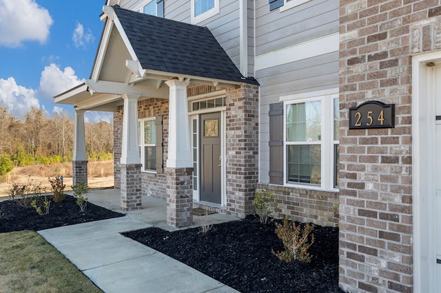 property entrance with brick siding, roof with shingles, and covered porch