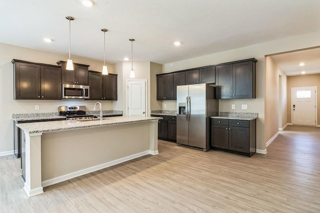 kitchen with appliances with stainless steel finishes, dark brown cabinetry, light hardwood / wood-style floors, pendant lighting, and a kitchen island with sink