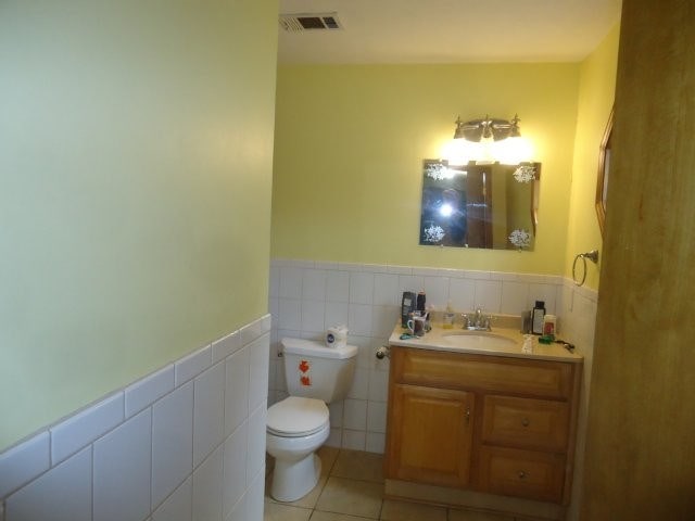 half bathroom with tile patterned floors, toilet, visible vents, and wainscoting