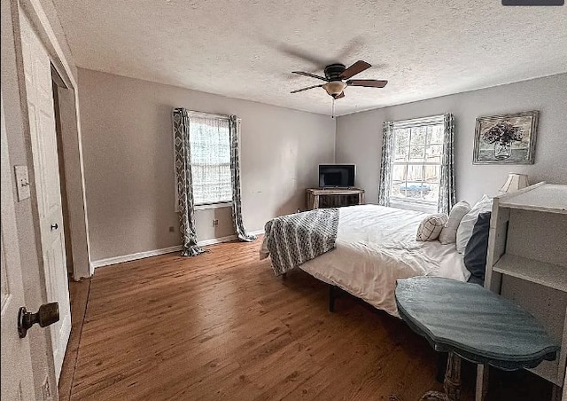 bedroom featuring a textured ceiling, multiple windows, baseboards, and wood finished floors