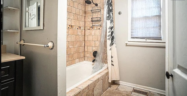 full bathroom featuring stone tile flooring, visible vents, tiled shower / bath, and baseboards