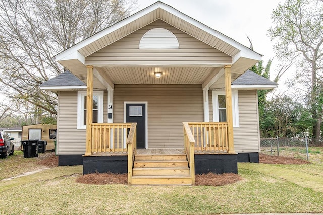 view of front facade featuring covered porch, a front lawn, and fence