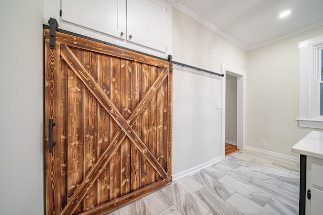 interior space featuring white cabinetry, a barn door, crown molding, and baseboards