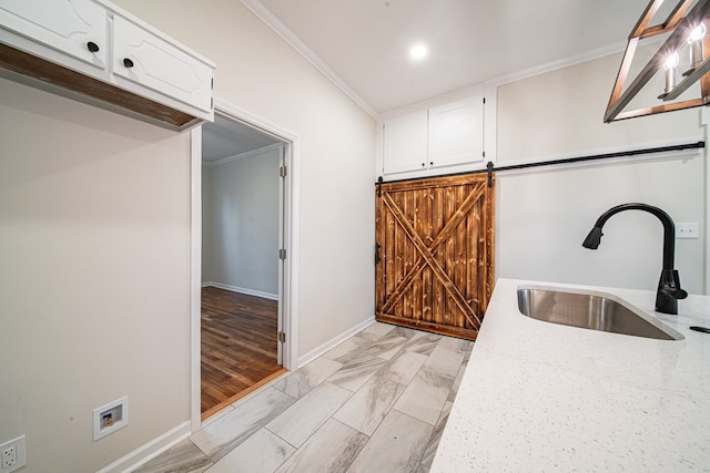 kitchen with ornamental molding, a sink, light stone counters, a barn door, and white cabinets