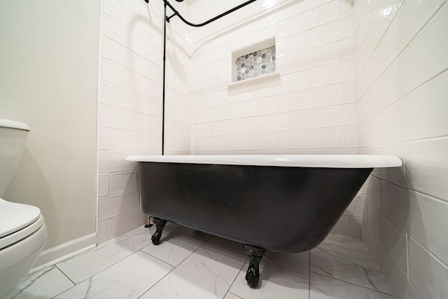 bathroom featuring toilet, baseboards, marble finish floor, and a freestanding bath