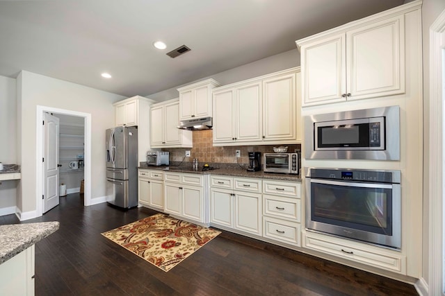 kitchen with visible vents, under cabinet range hood, decorative backsplash, appliances with stainless steel finishes, and dark wood-style floors