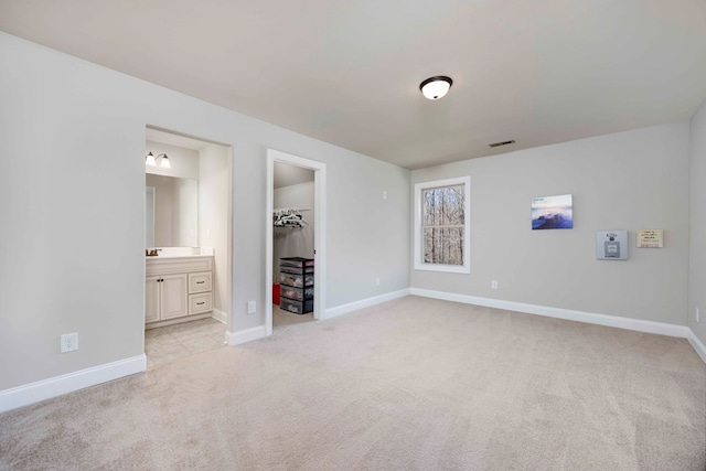 unfurnished bedroom featuring baseboards, ensuite bath, a spacious closet, a closet, and light colored carpet